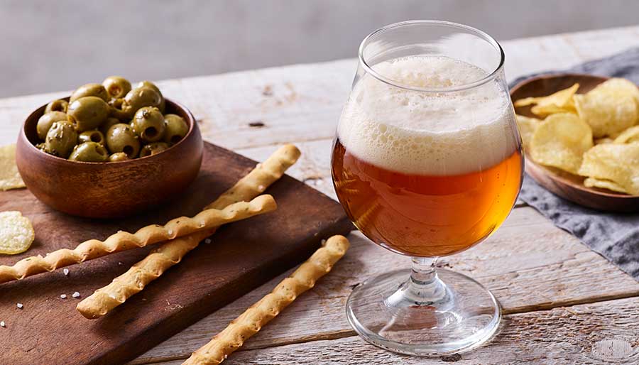 Table with a glass of beer, olives, bread sticks, chips