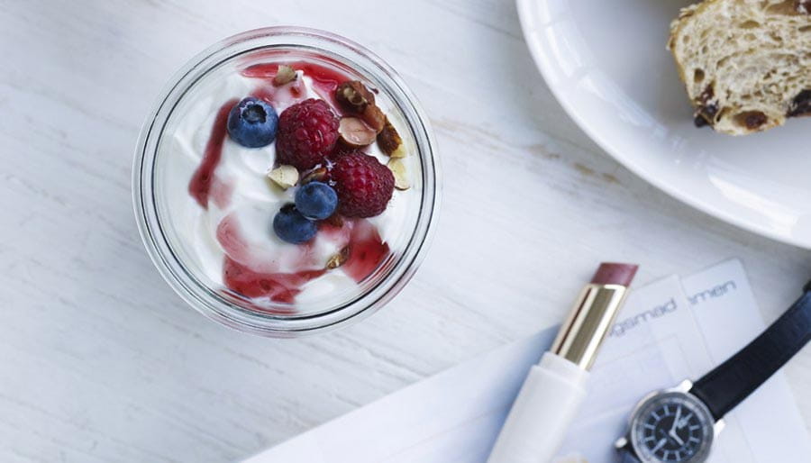 Yogurt with berries next to lipstick and watch