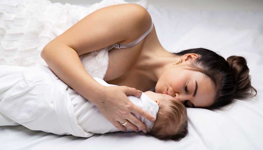 Mother-kissing-sleeping-baby-infant-in-bed